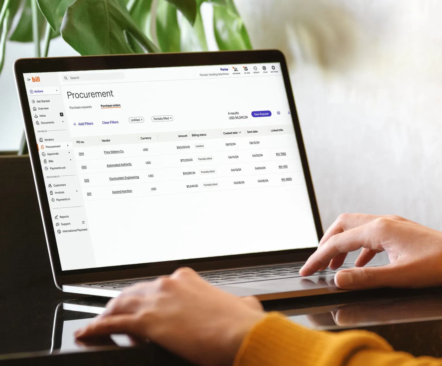 A person using a laptop displaying a BILL procurement dashboard with a list of financial transactions.