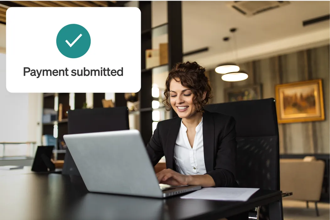 Smiling woman at table in a modern office using laptop, with "Payment submitted" notification overlayed.
