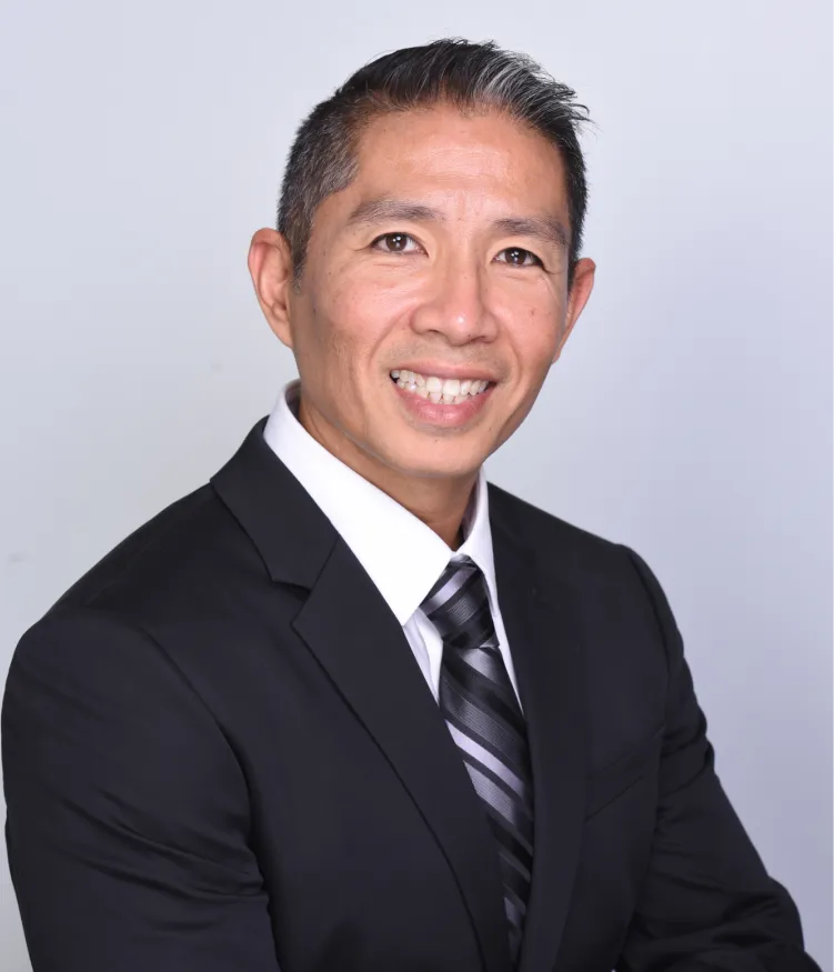 Smiling man in a black suit, white shirt, and striped tie posing against a plain light background.
