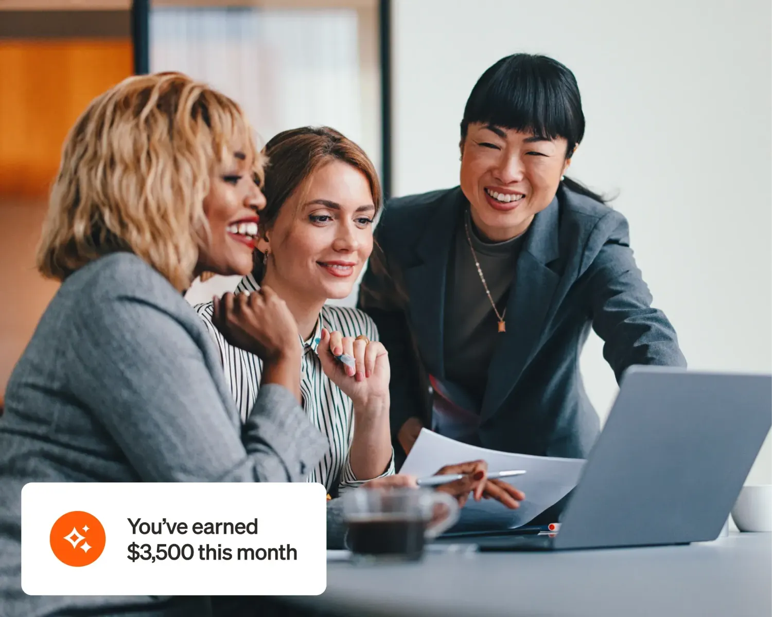 Three women smiling and looking at a laptop with a popup stating, "You've earned $3500 this month".