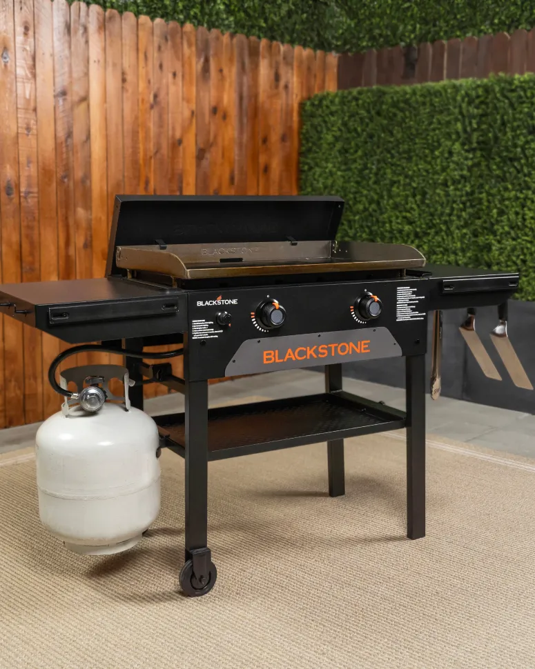 A Blackstone grill on a patio with wood fence and ivy covered wall in the background.