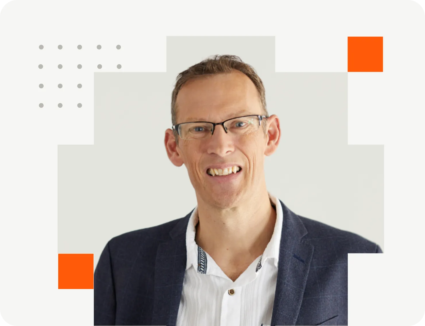Smiling man with short hair wearing glasses, a dark suit jacket, and white polo shirt in front of a neutral background.