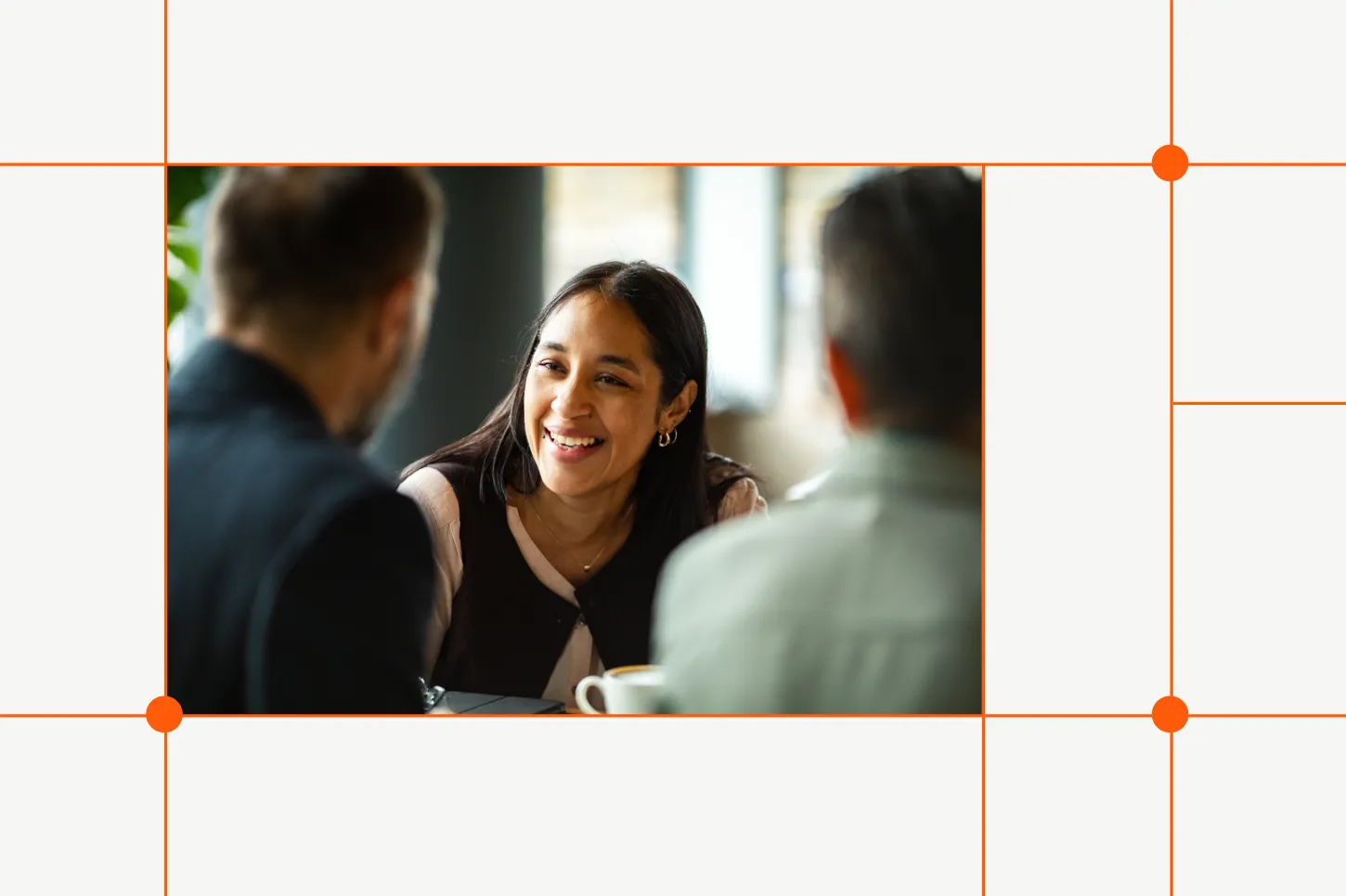 Smiling woman with long dark hair converses with two men in a bright office.