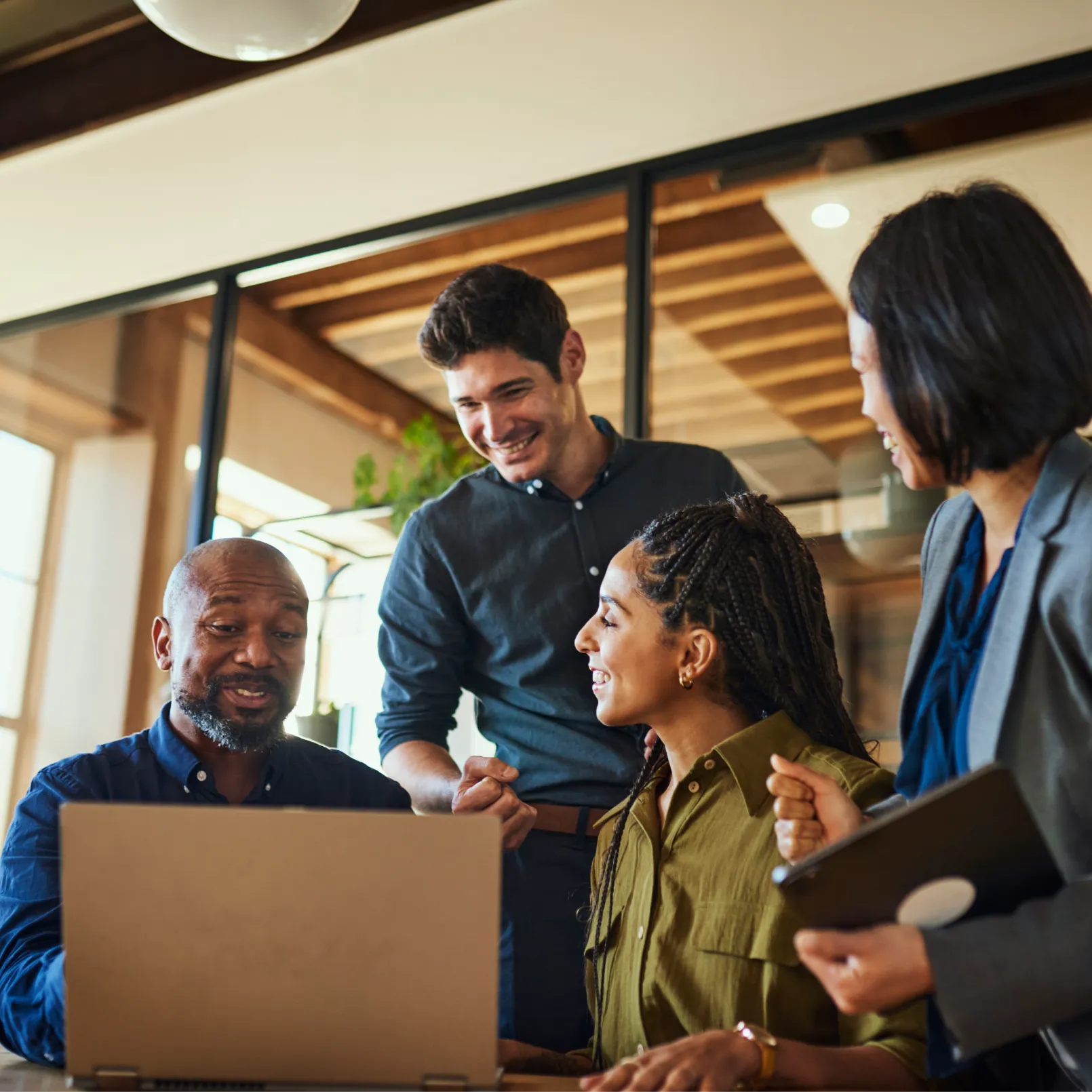 Four professionals gathered around a laptop on a table in a modern office setting.