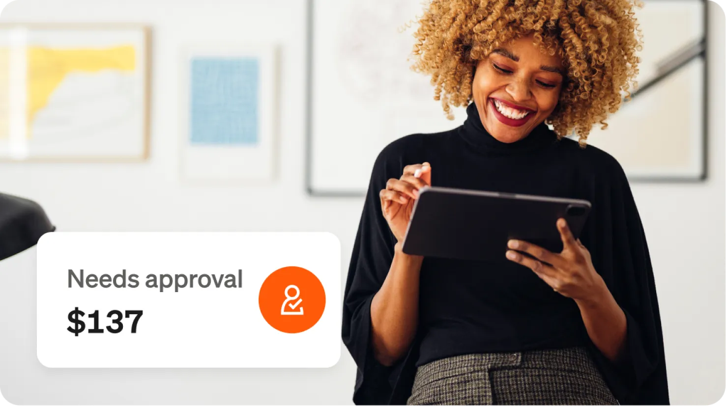 Smiling woman uses a tablet, framed wall art on a white wall behind her, notification "Needs approval $137" is overlaid beside her.