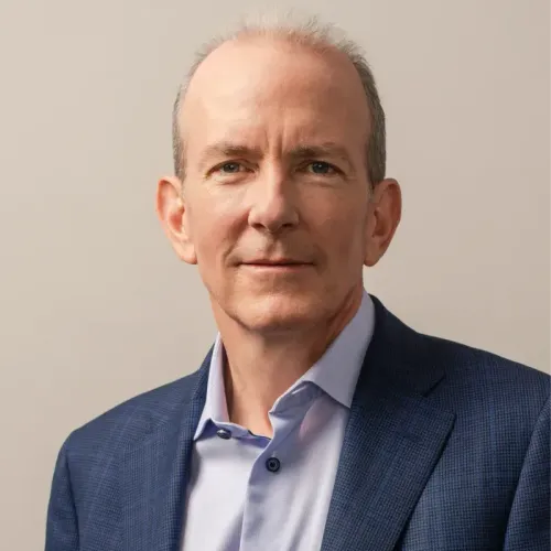 Headshot of a man in a light colored button-down shirt and navy suit jacket against a neutral background.