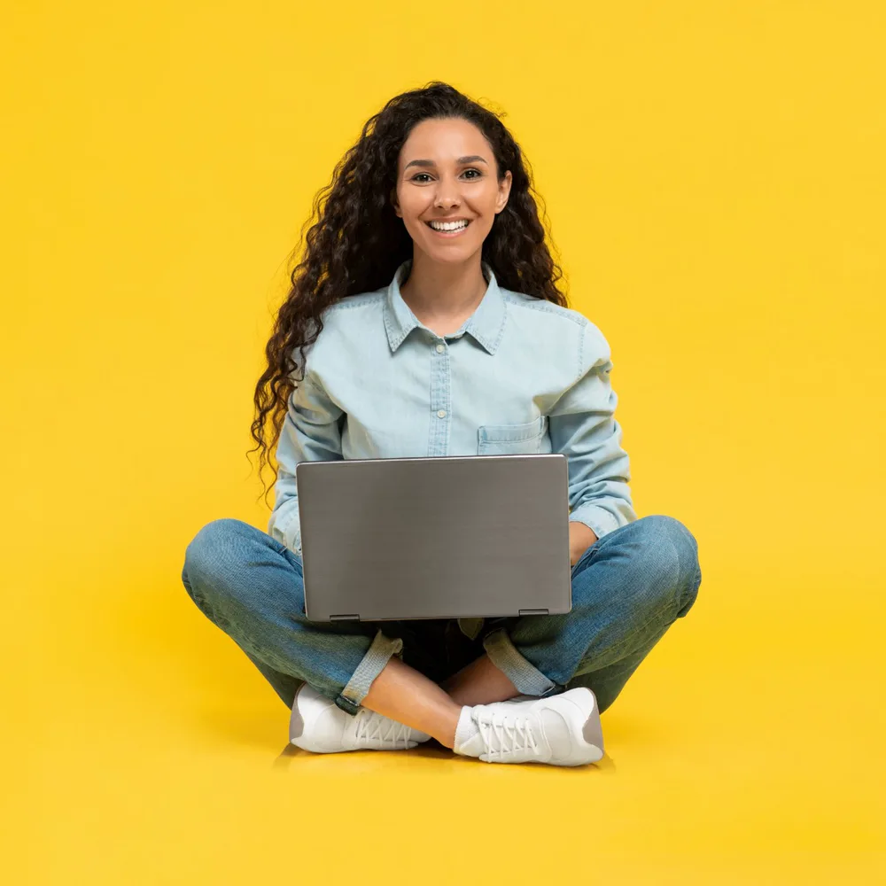 A smiling student sitting cross-legged with a laptop