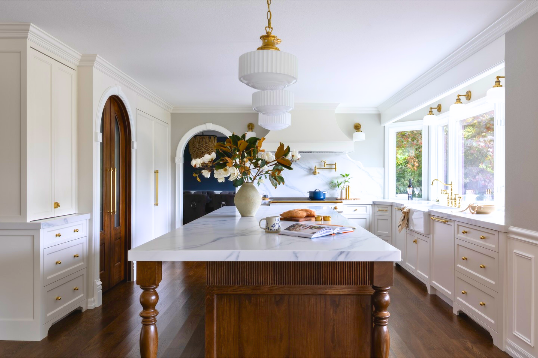 A white kitchen with a marble island and brass fixtures
