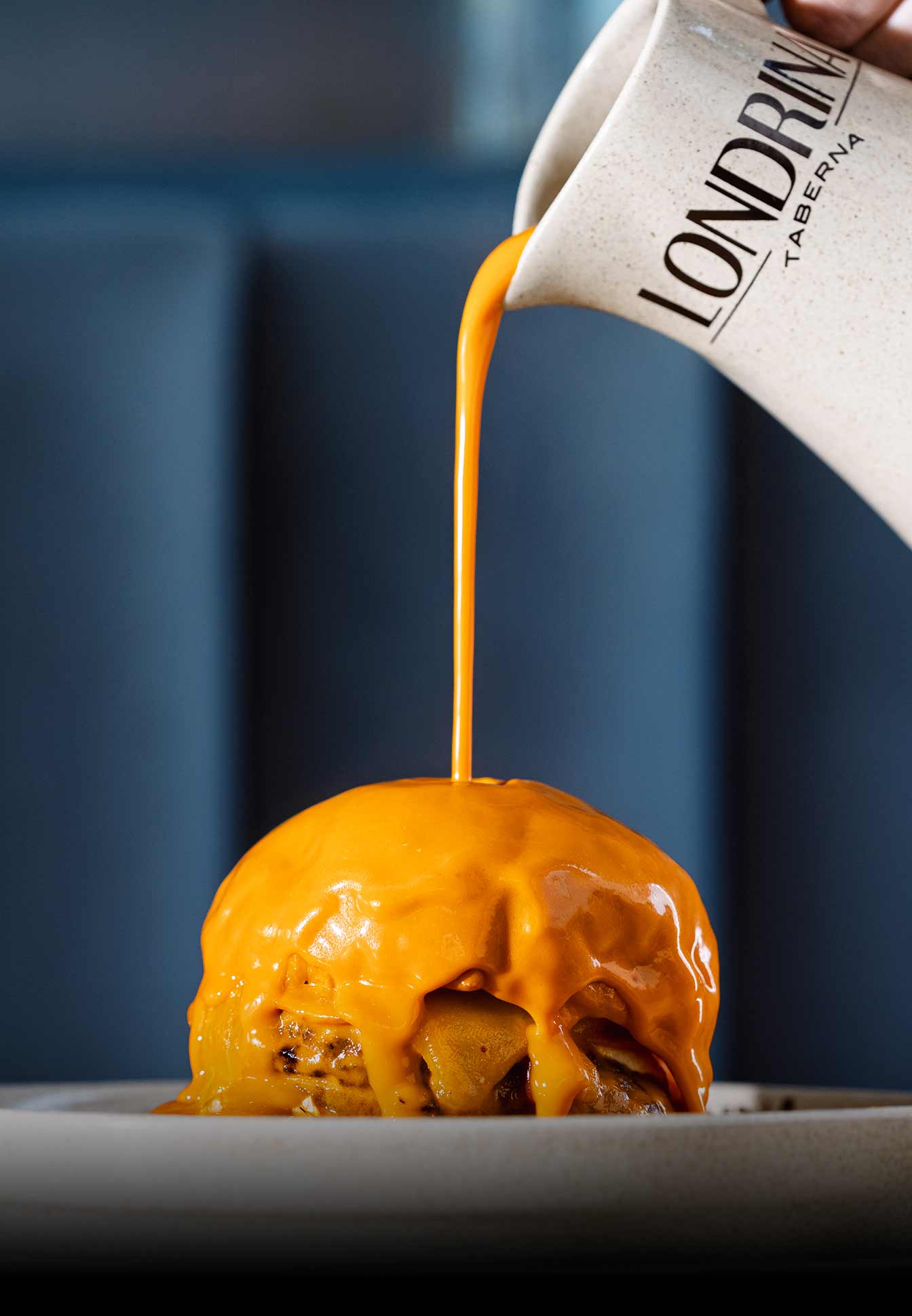 Molho de queijo laranja sendo derramado sobre um hambúrguer.