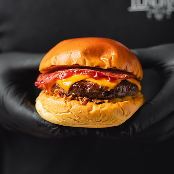 Hambúrguer com queijo, bacon e cebola crocante sendo segurado por uma mão.