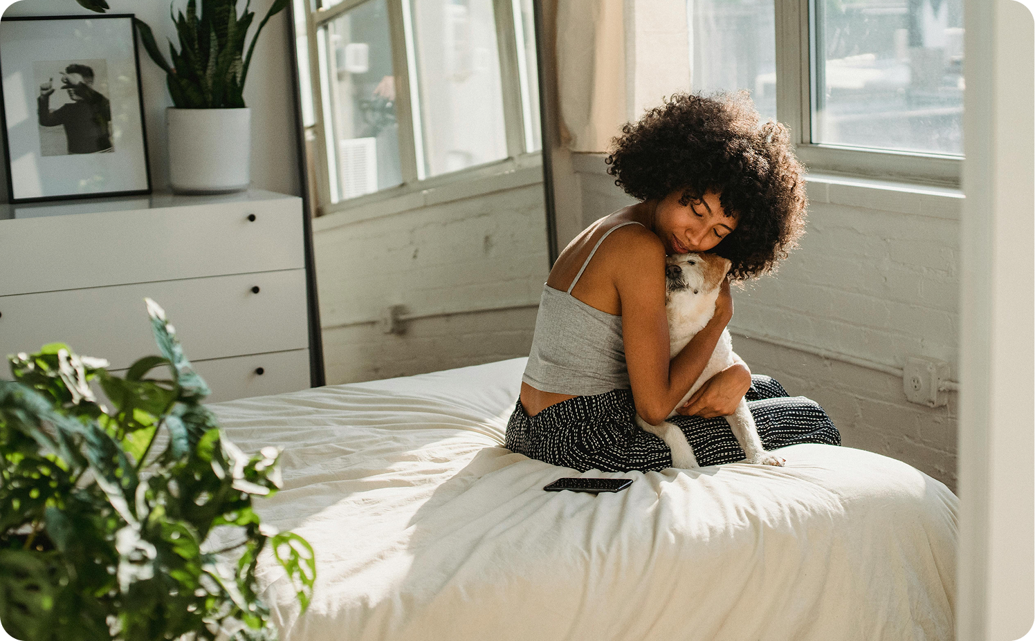 photo of woman hugging her dog in a sunny bedroom