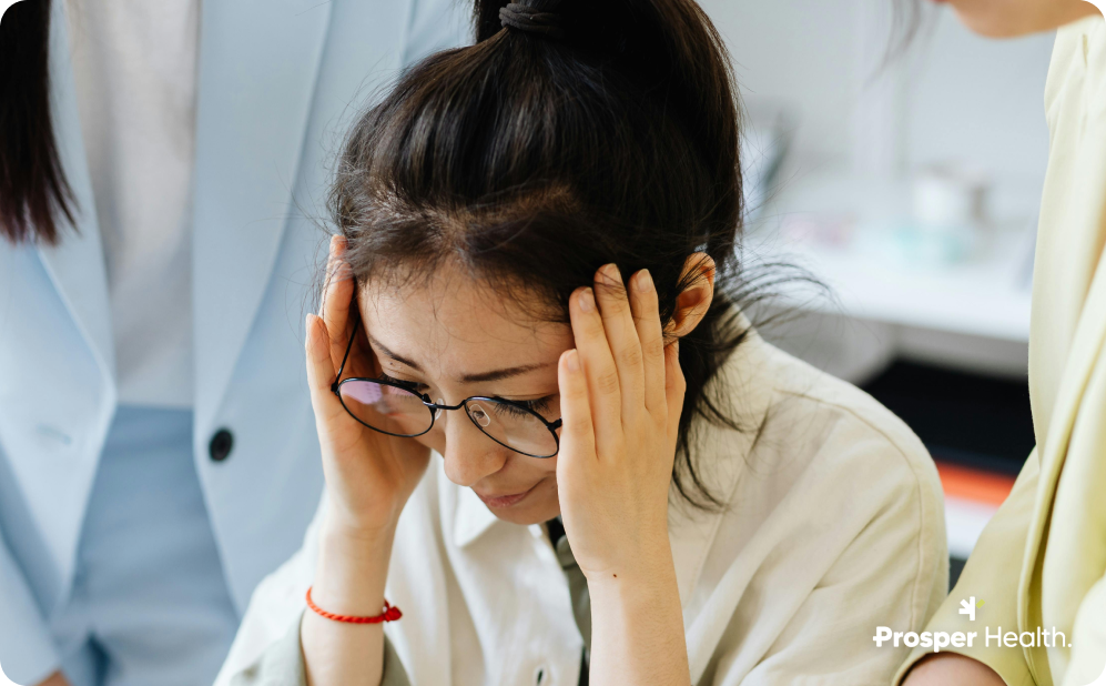 Asian woman with glasses holding her head in her hands