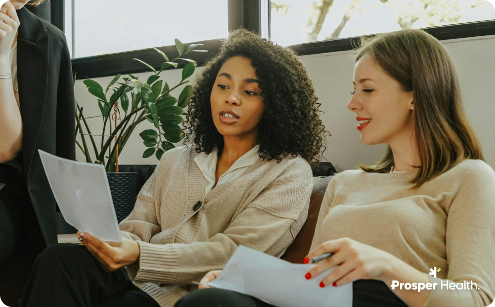Two women sitting on a couch reviewing some paperwork