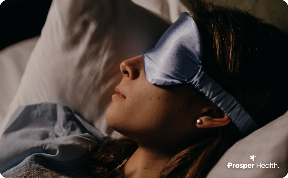 close up of woman lying in bed, presumably sleeping, wearing an eye mask.