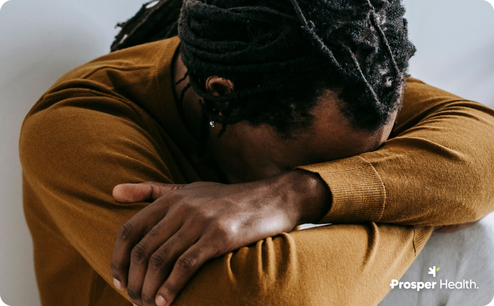 Person sitting with their head resting on their arms, conveying exhaustion or emotional distress.