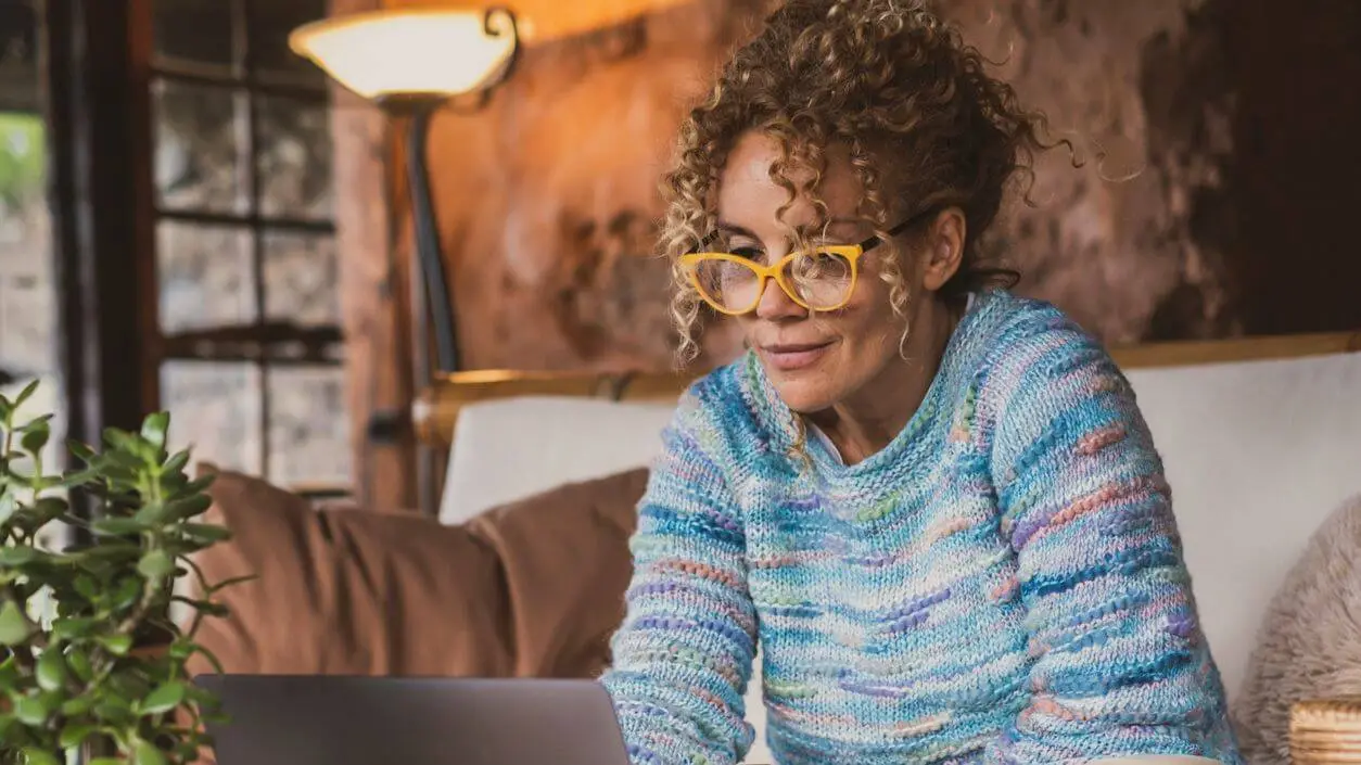 A woman wearing glasses is looking at a laptop.