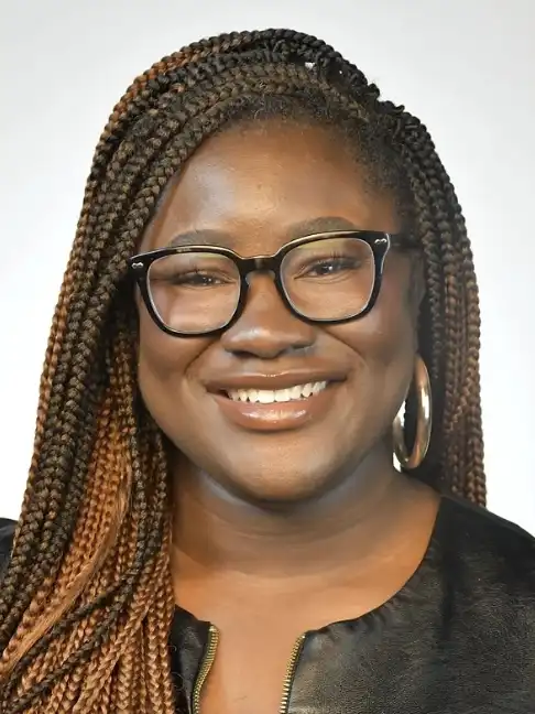 Jennifer Quaye-Hudson with braids wearing a black top with a zippered neckline and large hoop earrings.