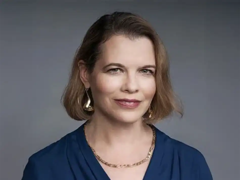 Ruth Halperin-Kaddari, wears a blue top, gold chain necklace, and large gold earrings.