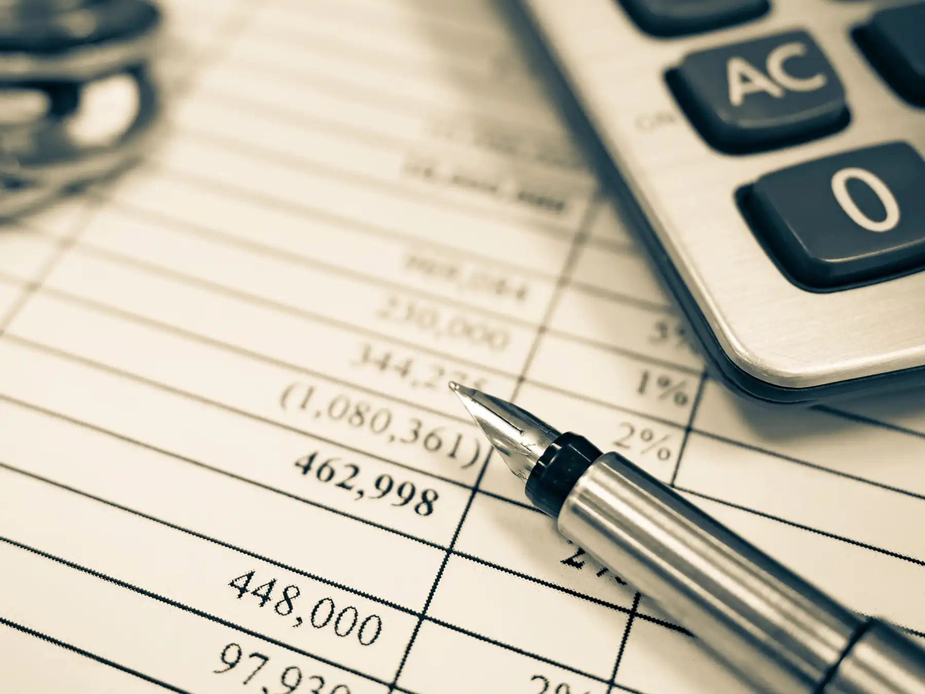 Close-up: fountain pen on a financial report with numbers, a negative balance, percentages, and a calculator in the background.