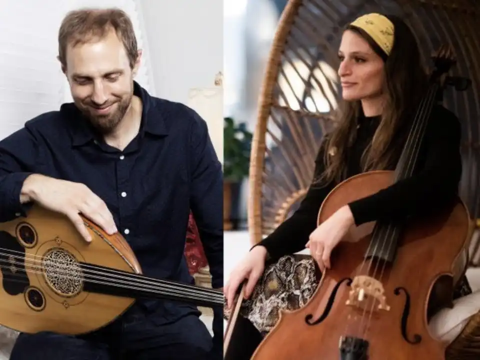 Portrait of musical duo ReynHartsik featuring a male musician holding an oud on the left and a female cellist seated in a wicker chair on the right.