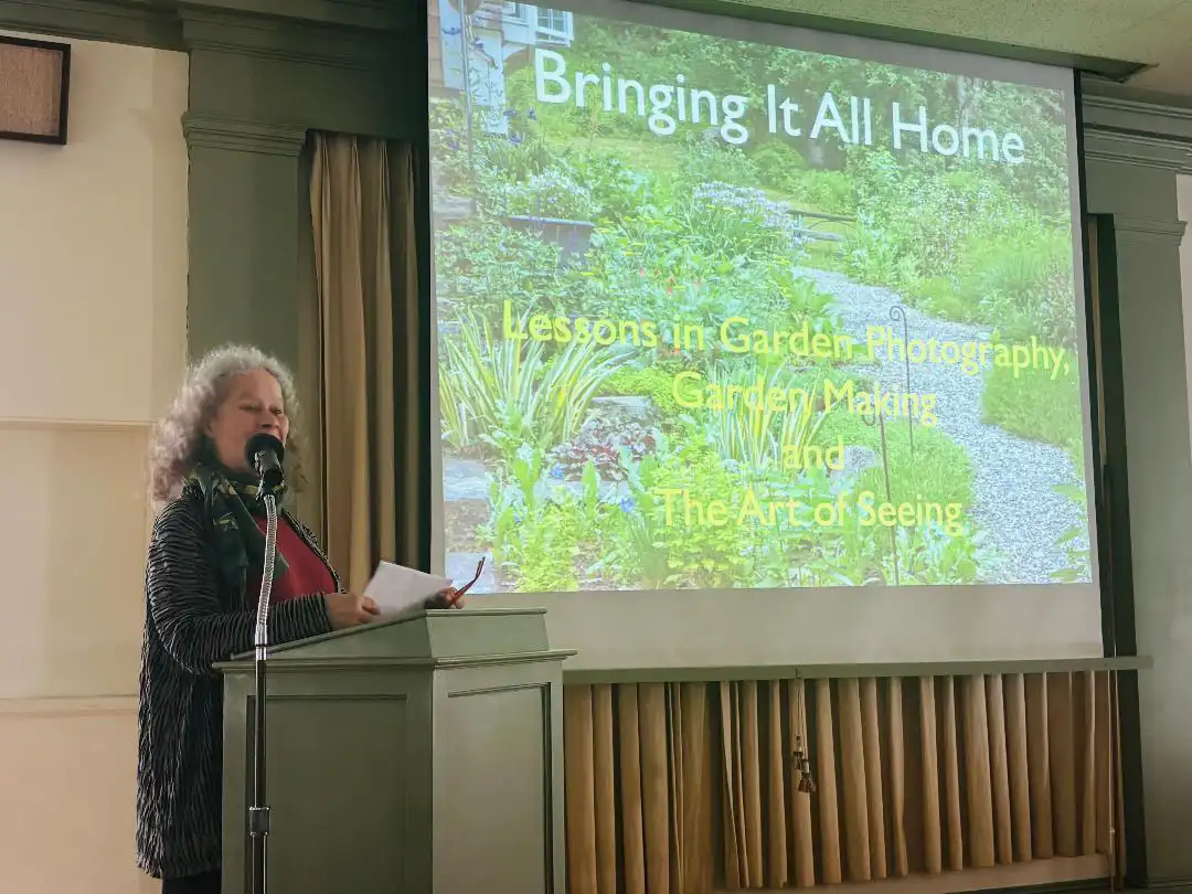 Speaker Karen Bussolini holding notes at a lectern in front of a presentation slide titled "Bringing It All Home."