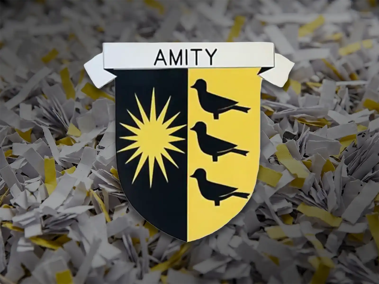 Alt text: A black and yellow heraldic shield with a 12-point sun, three blackbirds, and a ribbon reading AMITY rests on a pile of shredded paper.