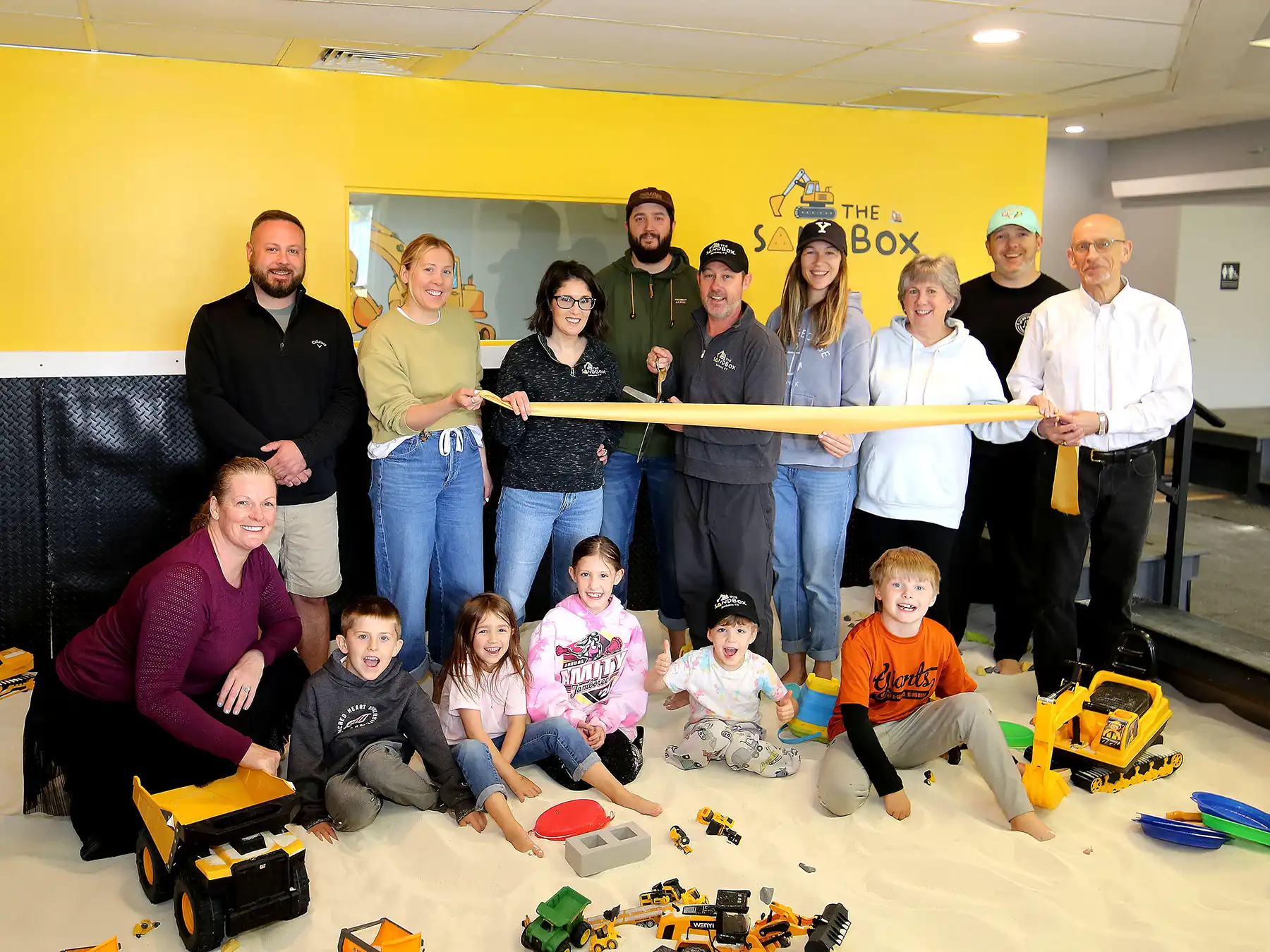 The Sandbox co-owners Dennis and Ryan Croteau hold a ribbon-cutting ceremony with family, friends, and Bethany officials in a large indoor sandbox.