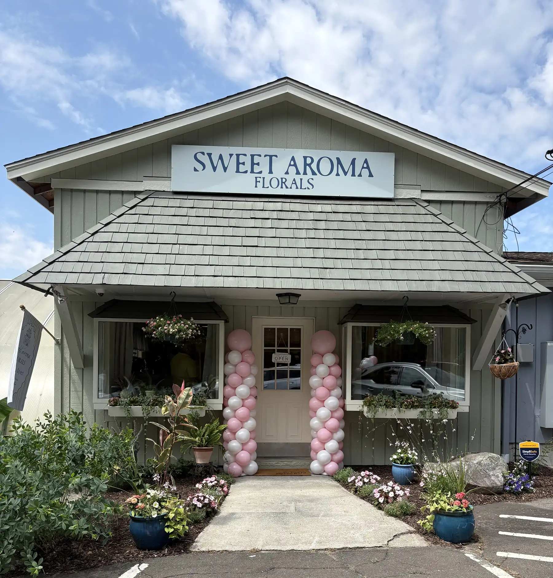 Exterior view of the new floral shop entrance decorated with festive pink and white balloon columns for its official grand opening celebration.