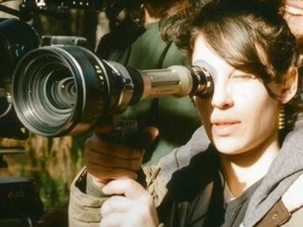 Filmmaker Rachael Mira Kliman looking through the viewfinder of a professional movie camera while directing on location.