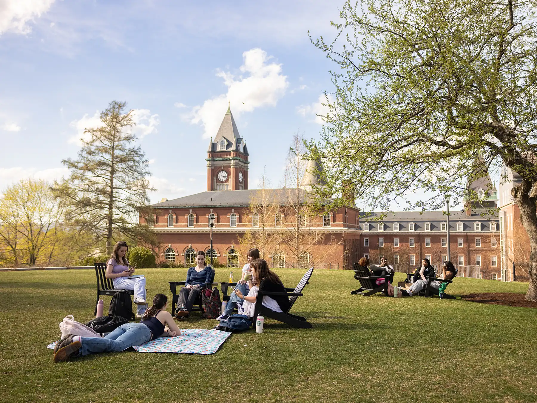 College of the Holy Cross students relaxing on the sunny campus lawn during a bright spring day in front of historic brick hall.