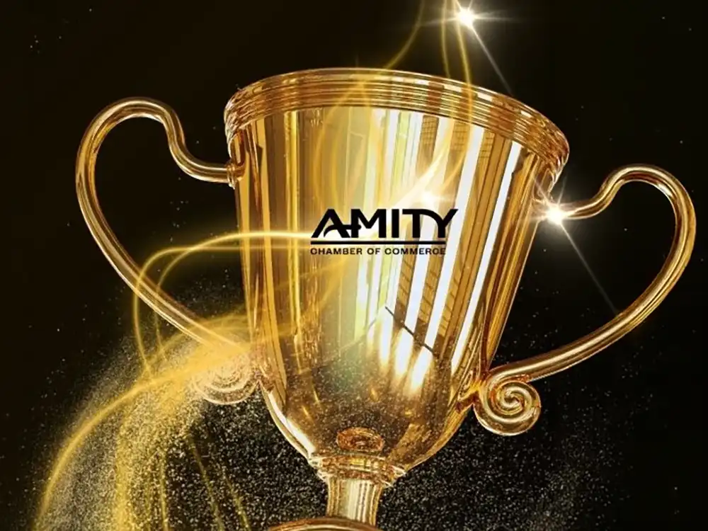 A shining golden trophy featuring the Amity Chamber of Commerce logo, surrounded by glowing light trails and gold dust against a dark background.