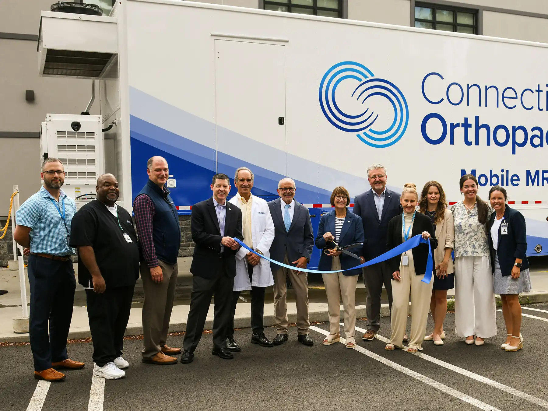 The Connecticut Orthopaedics team poses with a blue ribbon in front of the new Mobile MRI trailer during the ribbon cutting event.