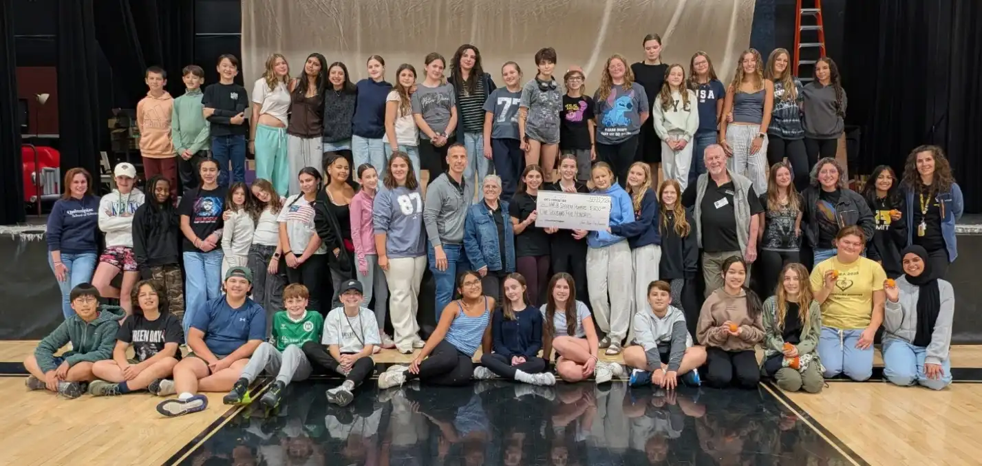 Bethany Spartan Players student cast and crew gather on stage holding an oversized grant check presentation from the Jamie Hulley Arts Foundation.