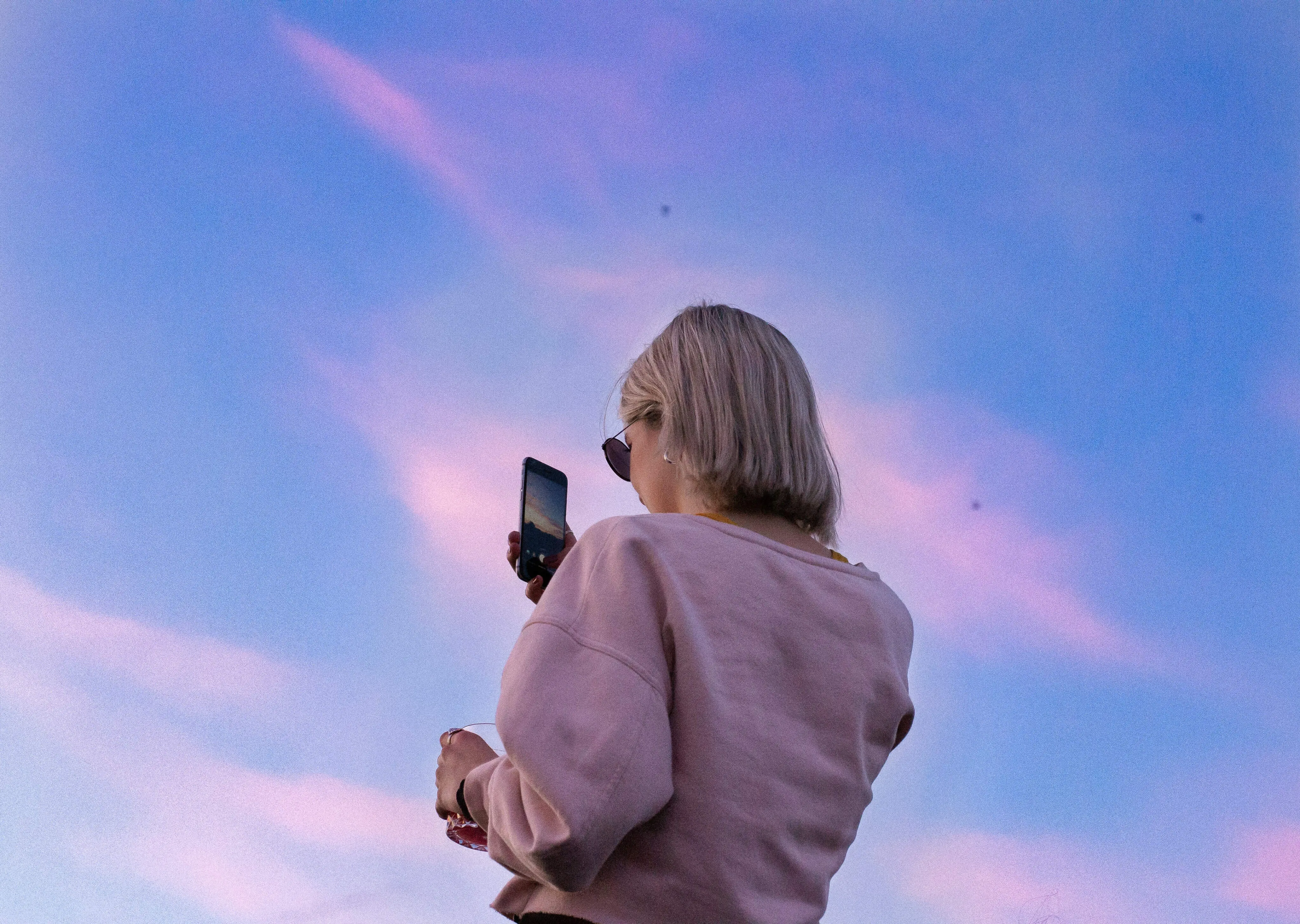 A woman in a pink sweater looking at a cell phone.
