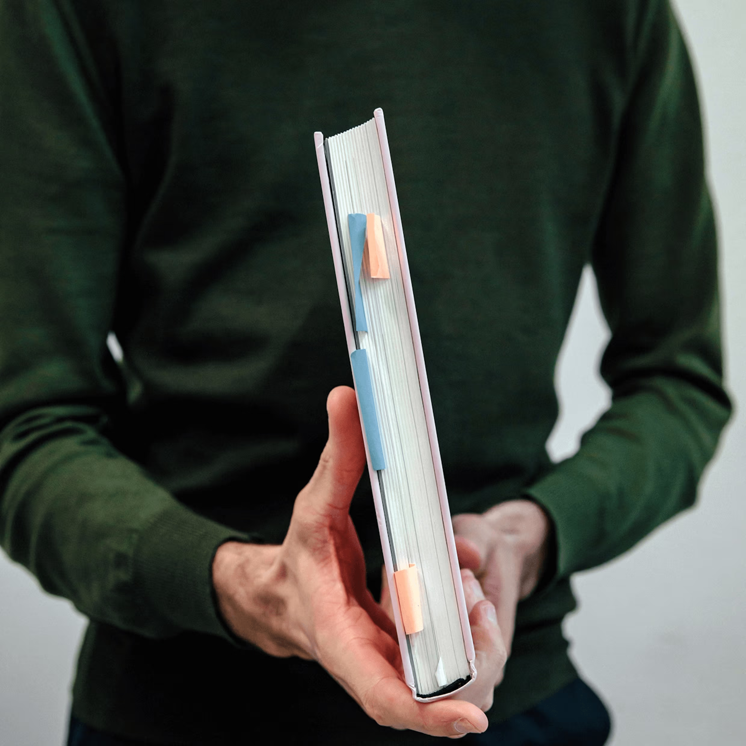 Person in dark green long-sleeve shirt holding a thick book with multiple colored sticky tabs.