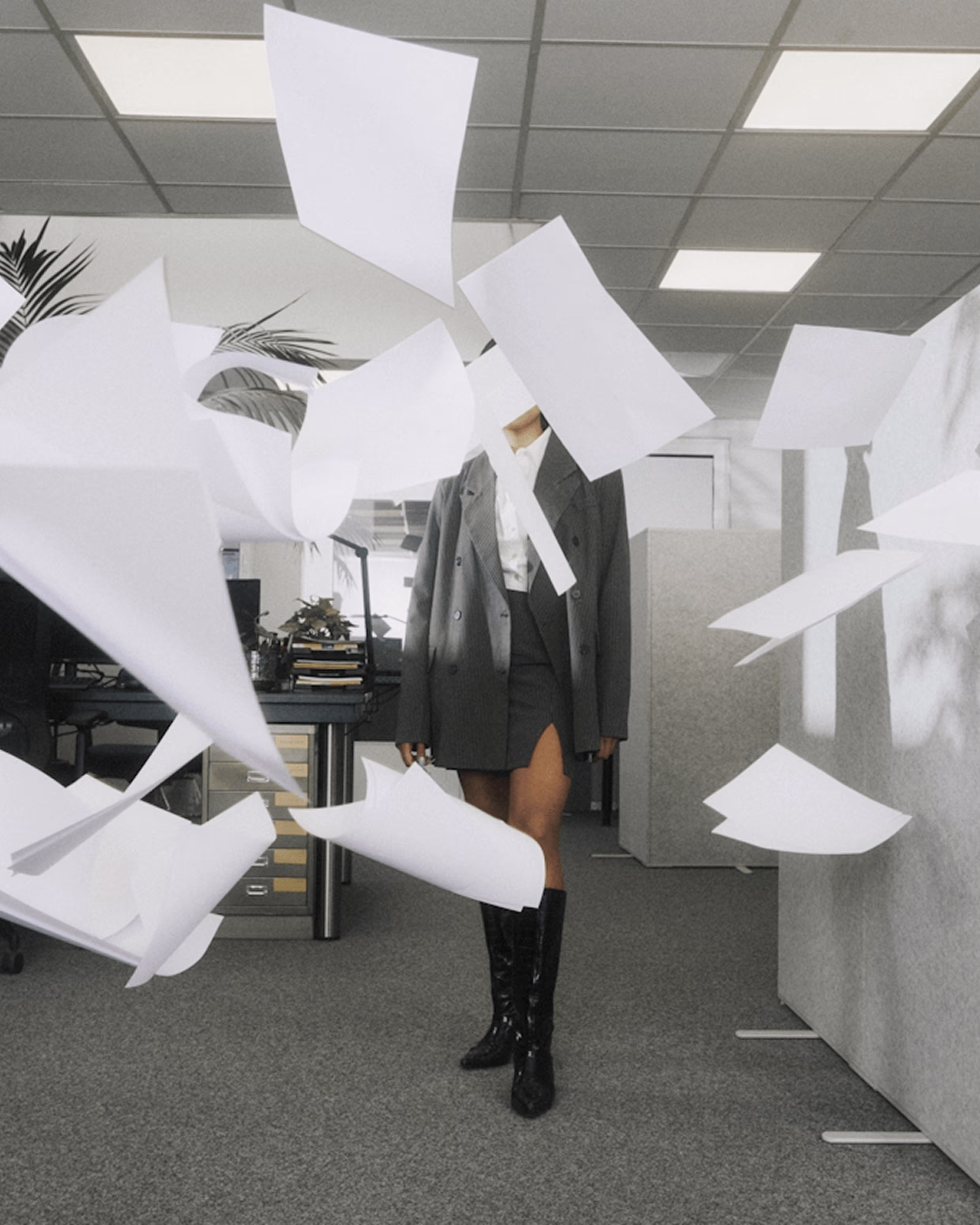 Person in business attire walking through an office with papers flying around them.
