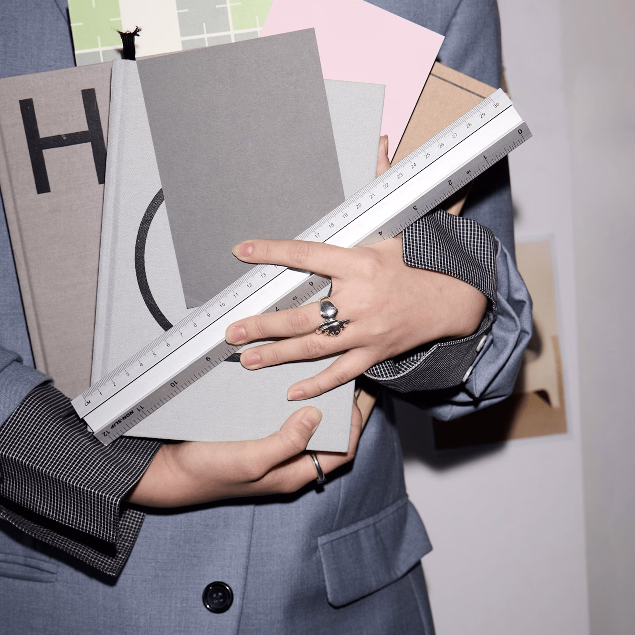 Person wearing a blue jacket holding several books and a metal ruler across their hands.