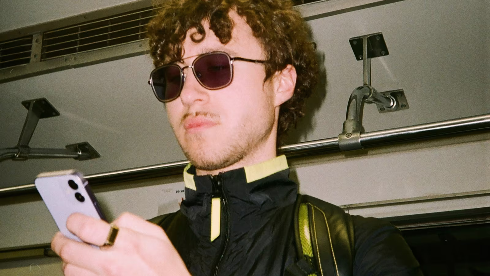 Young man with curly hair and sunglasses looking at his smartphone inside public transport.