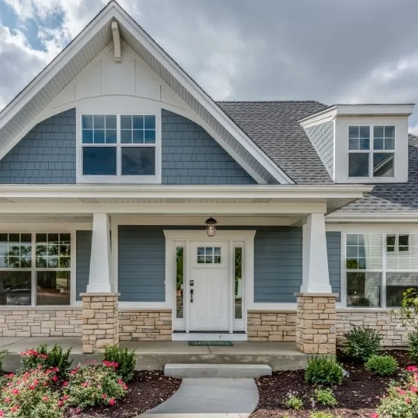 Blue-gray house with white trim, stone pillar bases, a covered porch, and a white front door with sidelights under a cloudy sky.