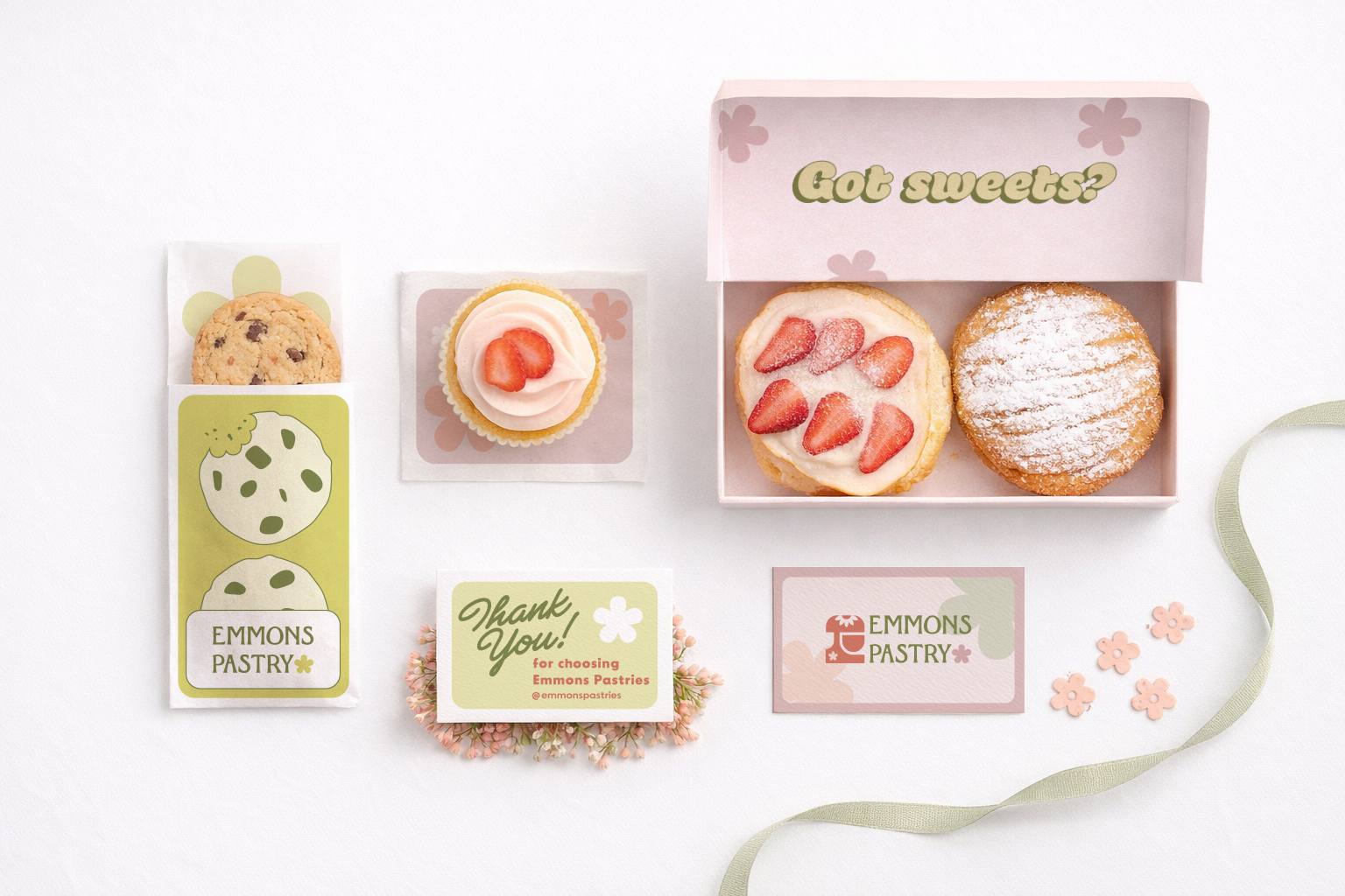 Pastries assortment including chocolate chip cookie in branded packaging, strawberry cupcake, box with strawberry and powdered sugar cookies, and two Emmons Pastry branded cards on white background.