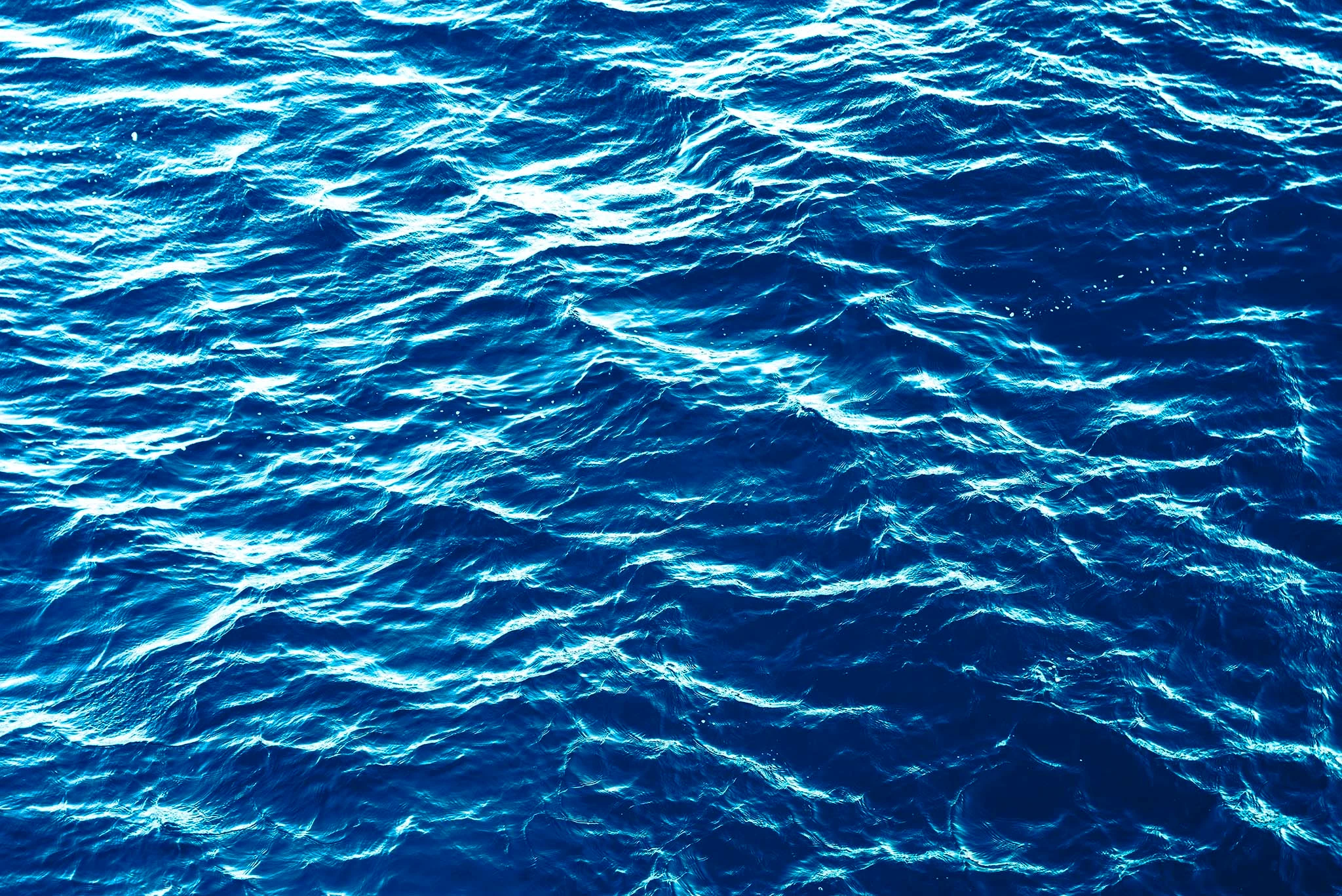 Deep blue ocean water surface with ripples and sunlight reflections.