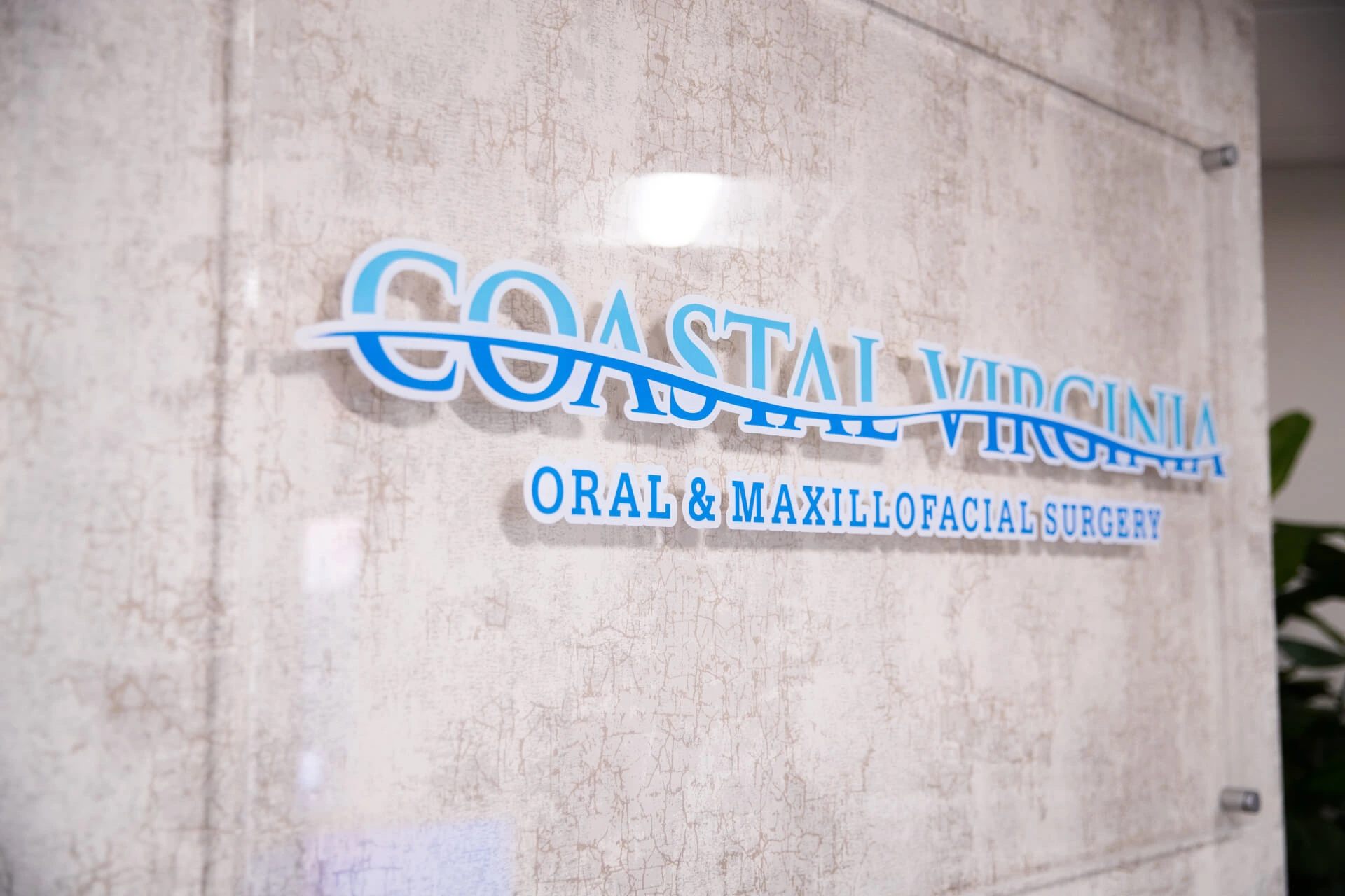 Coastal Virginia Oral & Maxillofacial Surgery logo sign on a textured wall.