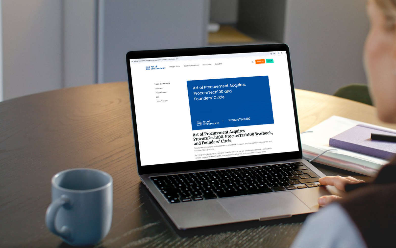 Person reading article about Art of Procurement acquiring ProcureTech100 and Founders’ Circle on a laptop at a desk with coffee mug.
