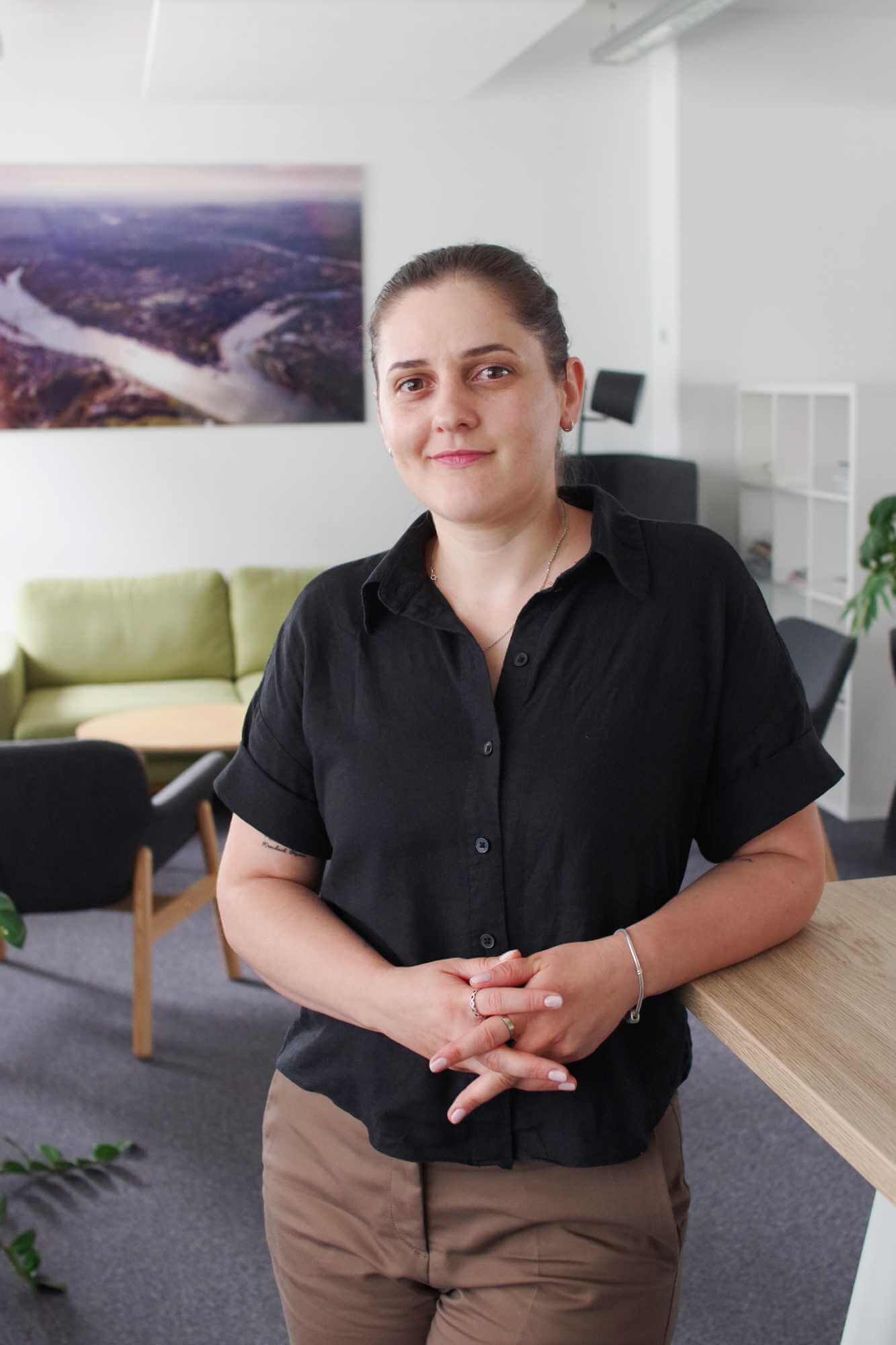 Saranda steht im Büro von ivoflow und lächelt in die Kamera, im Hintergrund Sitzbereich und modernes Arbeitsumfeld.