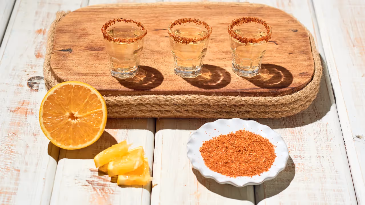 Three shot glasses with a chilli flake rim sitting on a chopping board. 