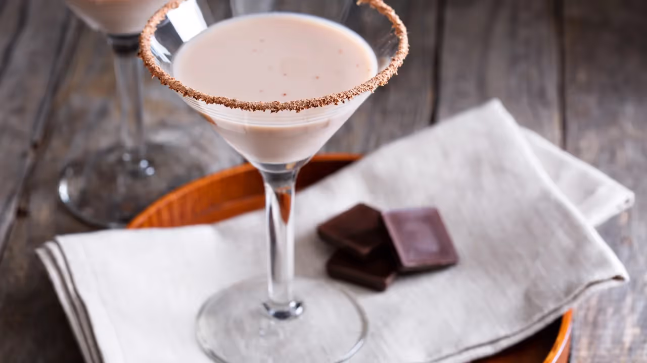 A chocolate martini stands next to 3 squares of dark chocolate.
