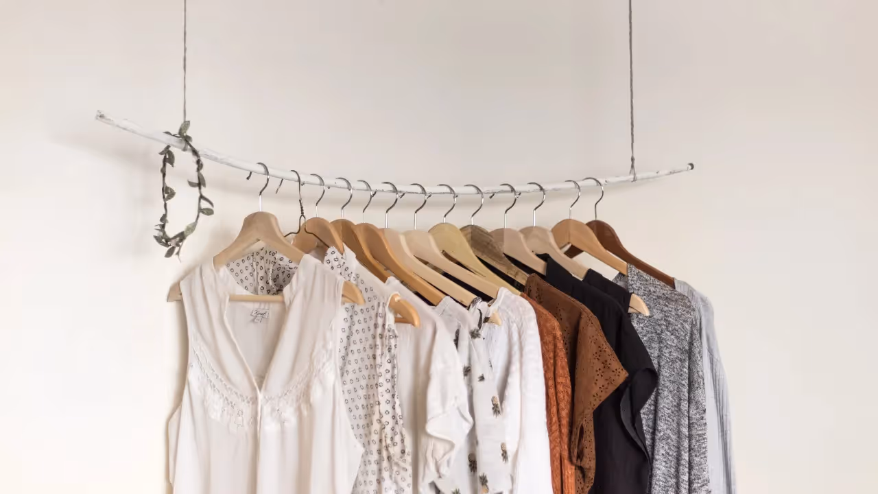 A hanging rail of neutral coloured clothes sits infront of a white wall. 