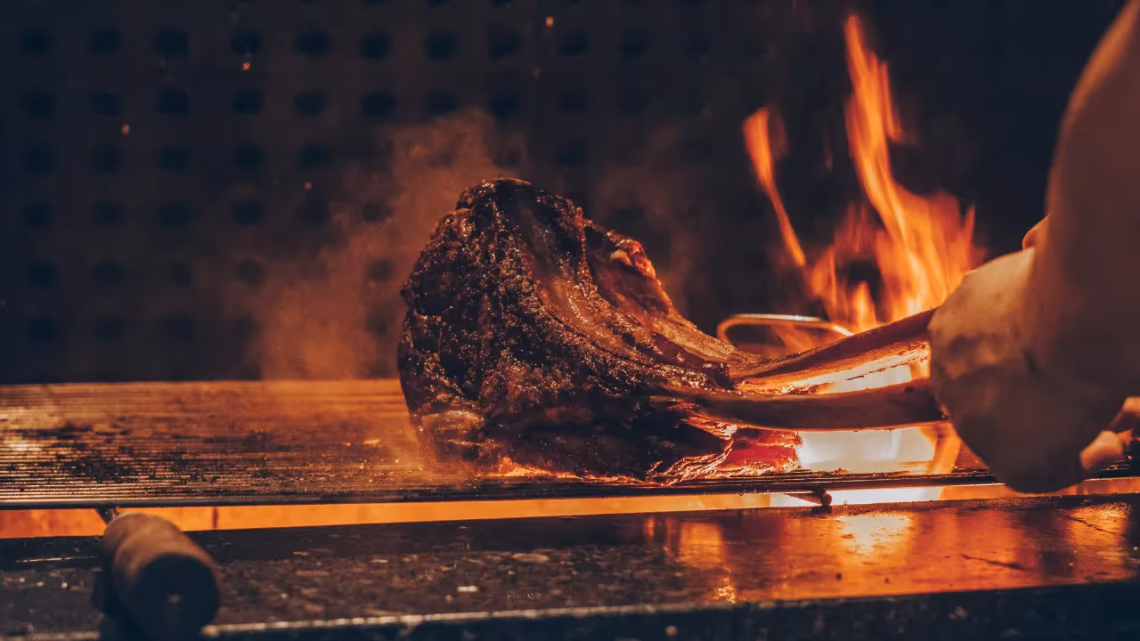 Meat on the bone is being cooked on a BBQ, on live flames. 