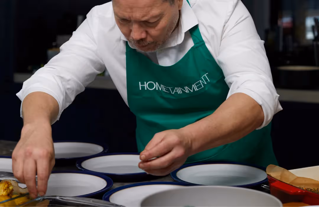 A professional HOMETAINMENT chef in London meticulously plating a gourmet dish, bringing fine dining experiences to private homes. A bespoke at-home culinary service, perfect for exclusive events and intimate gatherings.