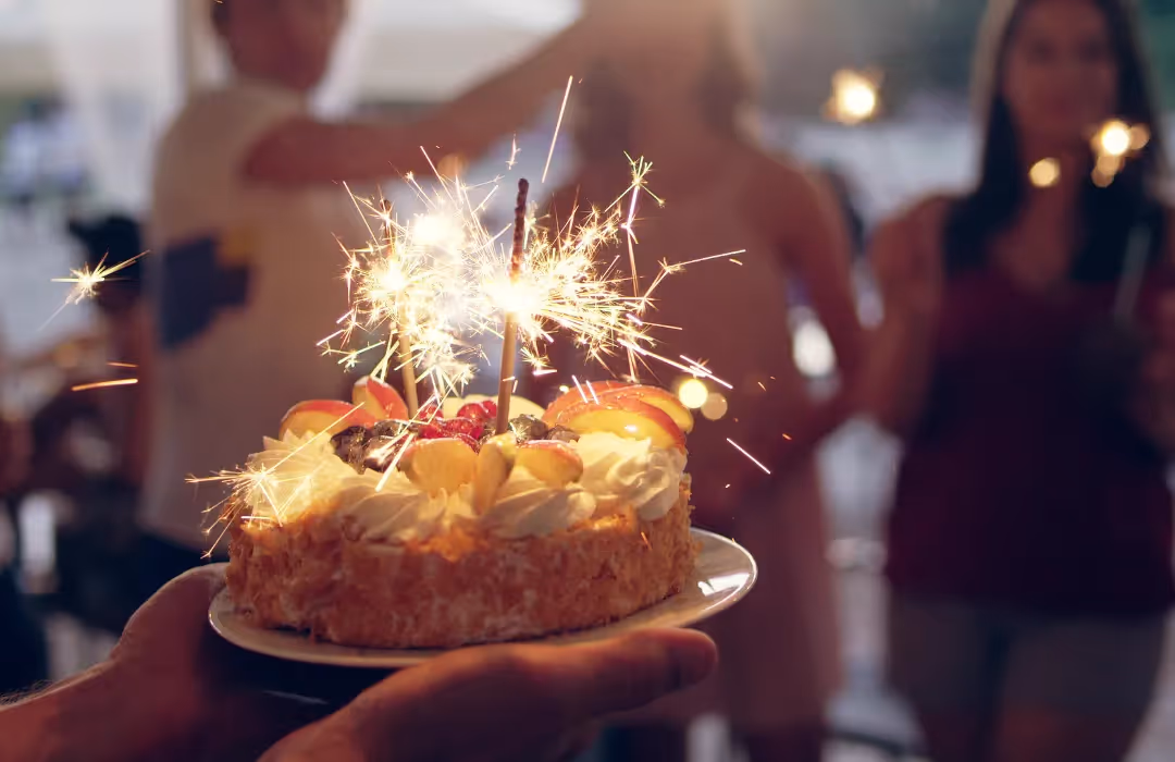 A beautifully decorated birthday cake with sparklers, surrounded by friends celebrating in a warm, festive atmosphere. A bespoke HOMETAINMENT experience in London, perfect for private parties, special occasions, and personalised home events.